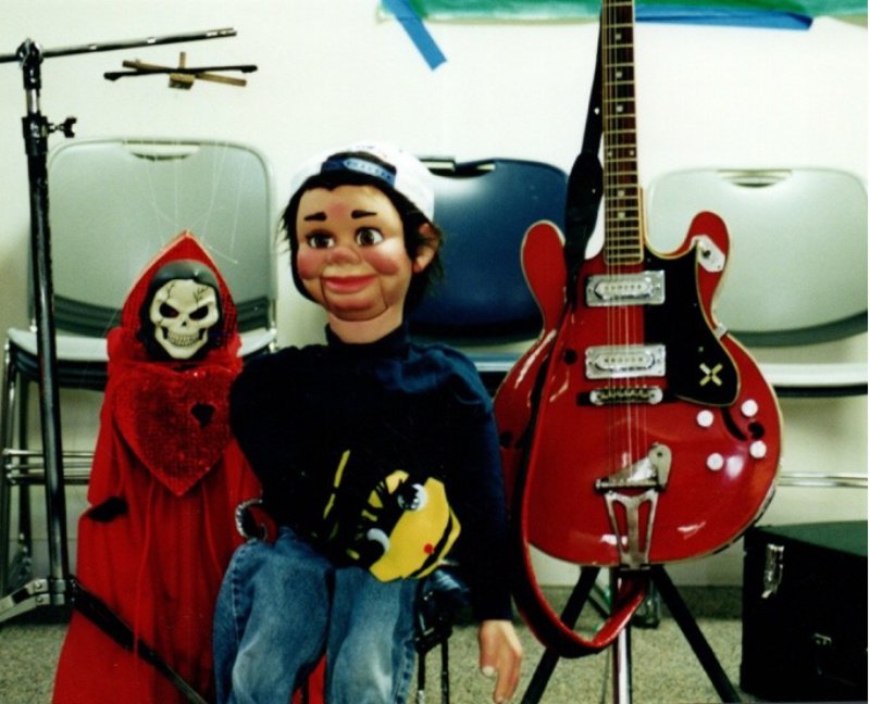Boy vent figure or dummy, beside a red guitar and red marionette.